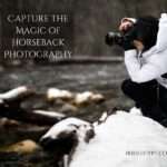 A photographer wearing a white winter jacket and black pants crouches on a snow-covered rock while taking photos in falling snow. Text overlay reads 'CAPTURE THE MAGIC OF HORSEBACK PHOTOGRAPHY' with 'IRIDEEGYPT.COM' in the bottom right corner