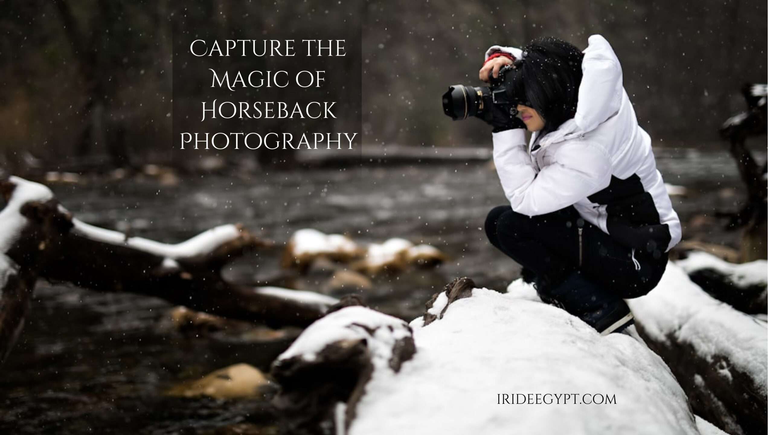 A photographer wearing a white winter jacket and black pants crouches on a snow-covered rock while taking photos in falling snow. Text overlay reads 'CAPTURE THE MAGIC OF HORSEBACK PHOTOGRAPHY' with 'IRIDEEGYPT.COM' in the bottom right corner